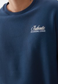 Felpa blu navy realizzata in morbido tessuto, dotata di colletto a girocollo a coste e logo ricamato bianco con la scritta "Authentic NYC Baseball League."