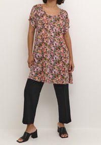 Blommig tunika i rosa, lila och grön på svart bakgrund, med lös passform, korta ärmar och gatherad halsringning. Matchas med svarta byxor.