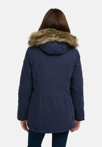 Tumesinine parkajakott kunstkarvaga voodriga kapuutsiga, mis on sileda tekstuuriga, keskmise pikkusega ja millel on nähtavad õmblusdetailid seljal.