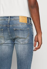 Jeans de ganga azul com um ajuste slim, apresentando costura contrastante, dois bolsos traseiros e um logótipo de pele na cintura.