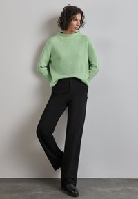 Minttivihreä ribbipaita ja mustat leveälahkeiset housut, joissa on korkea kaulus ja huomaamattomat sivunistukset, yhdistettynä mustiin jalkineisiin.