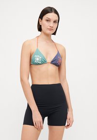 Bikini s trojuholníkovými košíkmi v tyrkysovej a námorníckej modrej s kvetinovým vzorom, skombinovaný s čiernymi šortkami s vysokým pásom vyrobenými z hladkého materiálu.