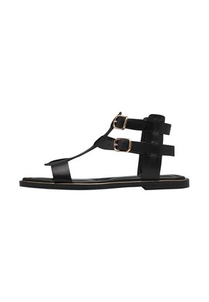 Sandales en cuir noir avec une semelle plate, comportant deux boucles réglables et un design en T. Minimaliste avec une apparence élégante.