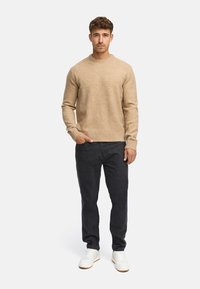 Beige gebreide trui, ronde hals, geribde manchetten, gecombineerd met donkerdenim en witte sneakers. Eenvoudig, strak ontwerp met een zachte textuur.