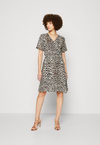 Robe portefeuille à imprimé léopard en beige et noir, à manches courtes, taille cintrée, jupe évasée, assortie à des sandales à talons beiges.