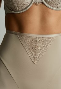 Shapewear se zvýšeným pasem s krajkovým lemem v neutrální béžové barvě, s hladkým materiálem a trojúhelníkovým krajkovým vzorem na vrchu.