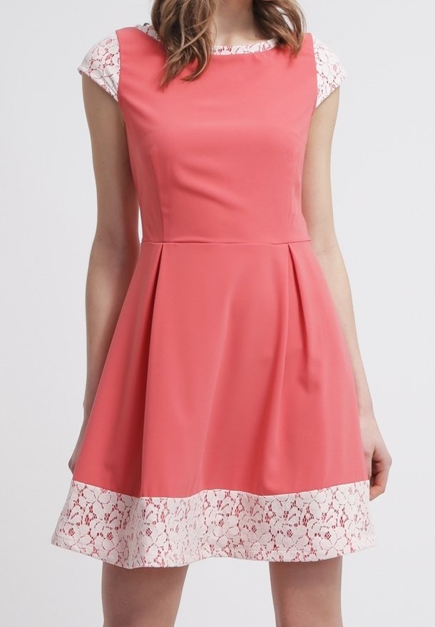 Bezrękawna sukienka w kolorze koralowym z białą koronką na dole i białymi koronkowymi krótkimi rękawami pod spodem.
