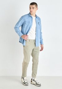 Jasnoniebieska koszula dżinsowa na białej koszulce, w połączeniu z jasnobeżowymi spodniami i czarno-białymi trampkami. Prosty fason, luźny krój.