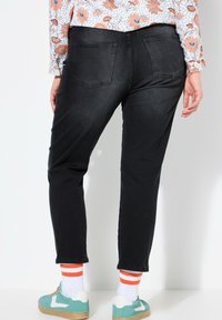 Pantalones de mezclilla negros con un corte ajustado, que cuentan con dos bolsillos traseros. Complementados con zapatillas teal y calcetines blancos con rayas naranjas.