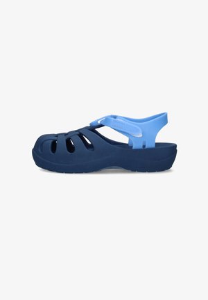 Sandalo blu navy con punta chiusa, cinturino alla caviglia regolabile azzurro chiaro e fori di ventilazione ai lati, mostrato di profilo.