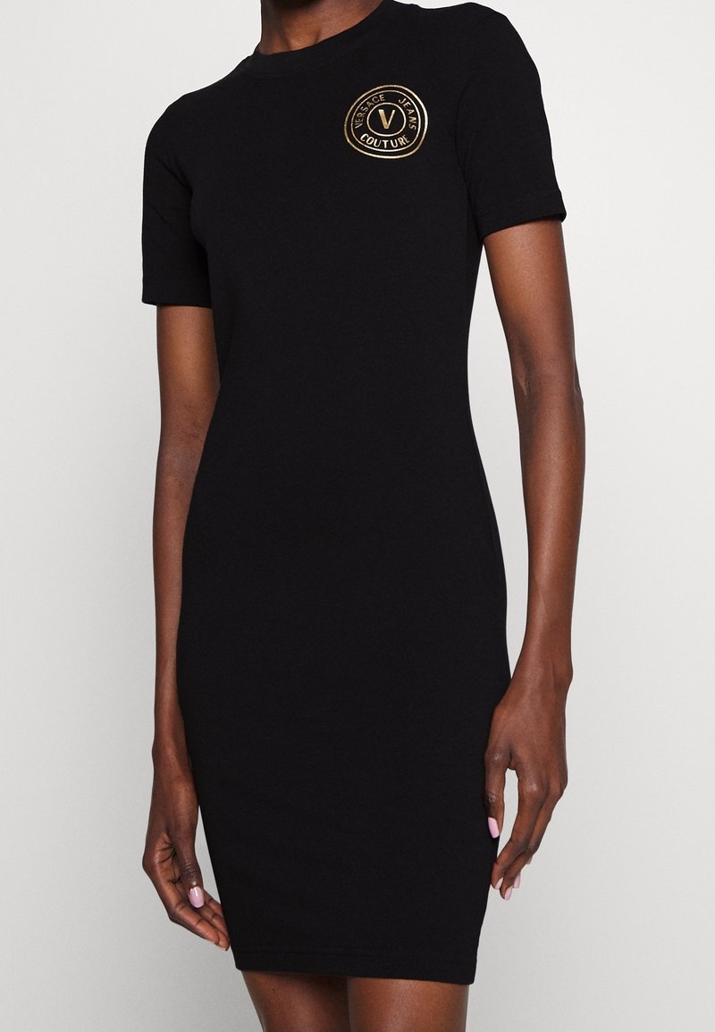 Svart kortärmad åtsittande klänning med rund halsringning och broderad guld-logotyp på bröstet. Slät tyg och knälång design.