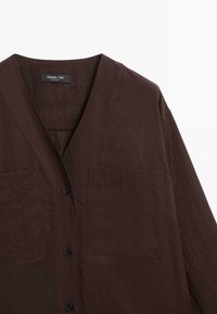 Brun skjorte med knapper og v-hals design, med to forlommer og et tekstureret stof. Enkel og minimalistisk stil.