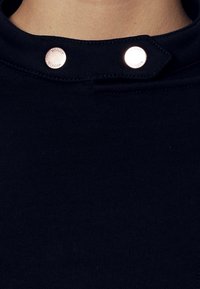 Tissu côtelé bleu marine avec un col montant, doté de deux boutons-pression métalliques au niveau du col pour la fermeture.