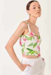 Kwiatowy crop top z białym tłem, zdobiony różowymi nadrukami orchidei i zielonymi liśćmi. Na cienkich ramiączkach i dopasowanym kroju.