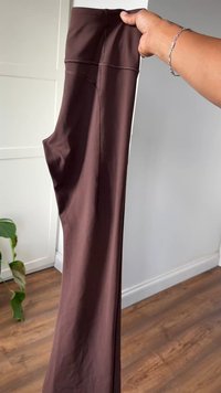 Leggings marroni, elasticizzati, con una texture liscia, vita alta e cuciture sottili. Tenuti in posizione verticale su uno sfondo neutro.