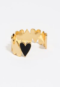 Anillo en forma de corazón en tono dorado con bordes alternos lisos y dentados, presentando un gran acento en forma de corazón negro en el centro. Textura metálica.