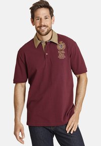 Maroon polo shirt with a beige collar, short sleeves, and embroidered rugby logo. Features a classic fit and soft cotton texture.