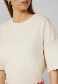 Crème-kleurig katoen t-shirt met korte mouwen, met een subtiele gele zonafbeelding op de borst, een gladde textuur en een ontspannen pasvorm.