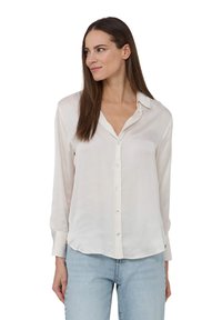 Blusa avorio chiaro realizzata in materiale setoso. Presenta un colletto a punta, chiusura frontale con bottoni e maniche lunghe. Texture liscia con vestibilità rilassata.