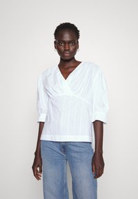 Hvit stripete bluse med dyp V-hals, puffete ermer og samlet midje. B�ært med lyseblå denimjeans med avslappet passform.