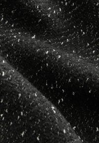 Tissu en laine noire avec des éclats blancs, montrant des fibres texturées, douces et légèrement bouclées en gros plan.