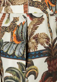 Fabric with tropical jungle print featuring a leopard, large green and brown leaves, and orange flowers on a light background.