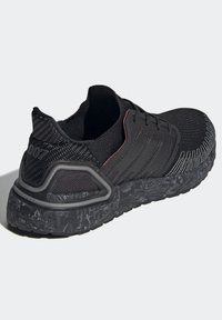 Baskets athlétiques noires avec semelle texturée, dessus en mesh, cadre de soutien au talon et bandes noires sur le côté sur un fond gris clair.