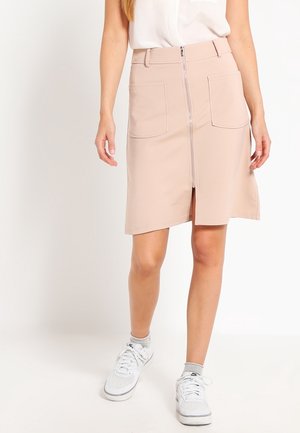 Lyserød knælængde nederdel i glat stof med en frontlynlås og to påsyede lommer. Bæres med en hvid top og sneakers.