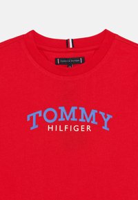 Κόκκινο βαμβακερό T-shirt με στρογγυλή λαιμόκοψη. Το κείμενο "TOMMY HILFIGER" είναι τυπωμένο σε μπλε και άσπρο χρώμα στο στήθος.