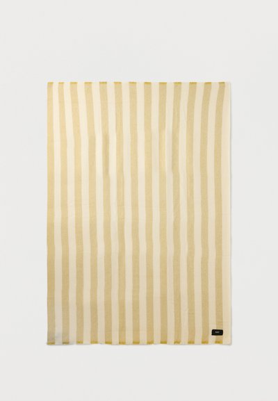 Ορθογώνιο υφαντό ύφασμα με ρίγες σε μπεζ και εκρού, με μια μικρή μαύρη ετικέτα στην κάτω δεξιά γωνία σε μονόχρωμο φόντο.