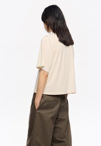 Top corto de color crema con ajuste relajado, textura suave y sutiles acentos en los hombros, combinado con pantalones de pierna ancha de color verde oscuro.