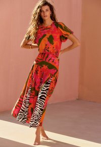 Lagana haljina koja sadrži vibrantne cvjetne i uzorke zebra pruga, kratke puf rukave, uski struk i duljinu do gležnjeva od tkanine u više boja.