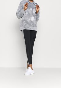 Szary hoodie w tie-dye z przednią kieszenią i regulowanym kapturem, zestawiony z czarnymi legginsami z szarymi paskami po bokach i białymi sneakerami.