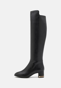 Bota de cuero negra hasta la rodilla con un diseño elegante, punta afilada, tacón cuadrado medio y acento de cadena dorada en el tacón. Textura suave.