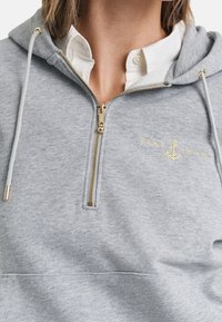 Grijze trui met een ritssluiting bij de hals, gouden details en een geborduurd ankerlogo. Gemaakt van zachte stof met een comfortabele pasvorm.