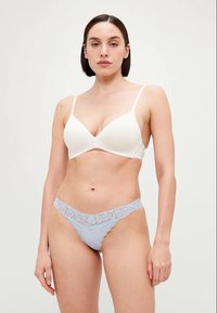 Weißer nahtloser Bra mit dünnen Trägern, kombiniert mit einem hellblauen Spitzen-Thong mit floralen Mustern und gewellten Kanten.