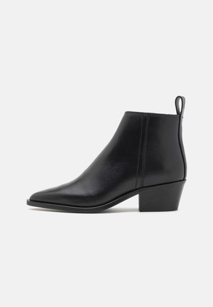 Bottines en cuir noir à bout pointu, talon carré bas et tirette à l'arrière. Texture lisse avec des coutures sur les côtés.