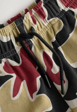 Shorts à cordon de serrage présentant un motif camouflage multicolore avec du noir, du rouge et du beige. Tissu doux avec une taille élastique et des surpiqûres contrastées.