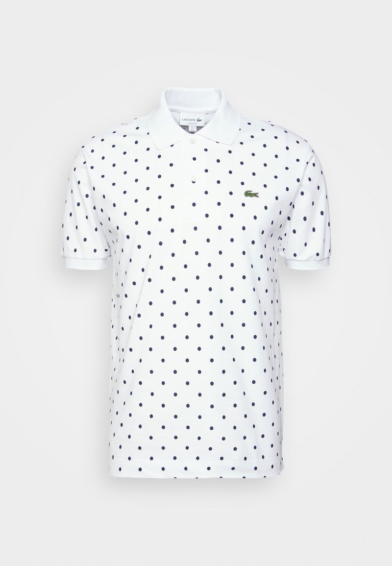 Polo blanc à manches courtes avec des pois bleu marine, un col, deux boutons et un petit logo crocodile vert sur la poitrine.