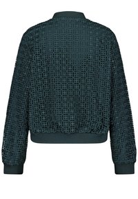Chaqueta bomber verde oscura con un patrón texturizado de círculos y cuadrados entrelazados, puños y dobladillo de canalé, construcción de tela ligera.