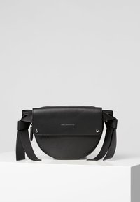 Sac en cuir noir en bandoulière de forme circulaire, avec des accents en ruban, fermeture à rabat et quincaillerie en argent. Logo situé à l'avant.