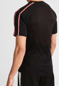 Camiseta deportiva negra con rayas rosas en los hombros y un panel trasero de malla, diseñada para comodidad y transpirabilidad.
