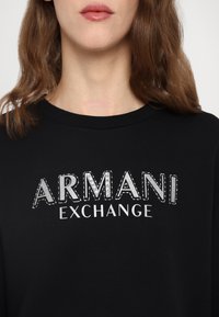 Zwarte sweatshirt met "ARMANI" en "EXCHANGE" in zilveren tekst, plus strasstenen accenten en geribbelde halslijn. Zachte katoen stof.