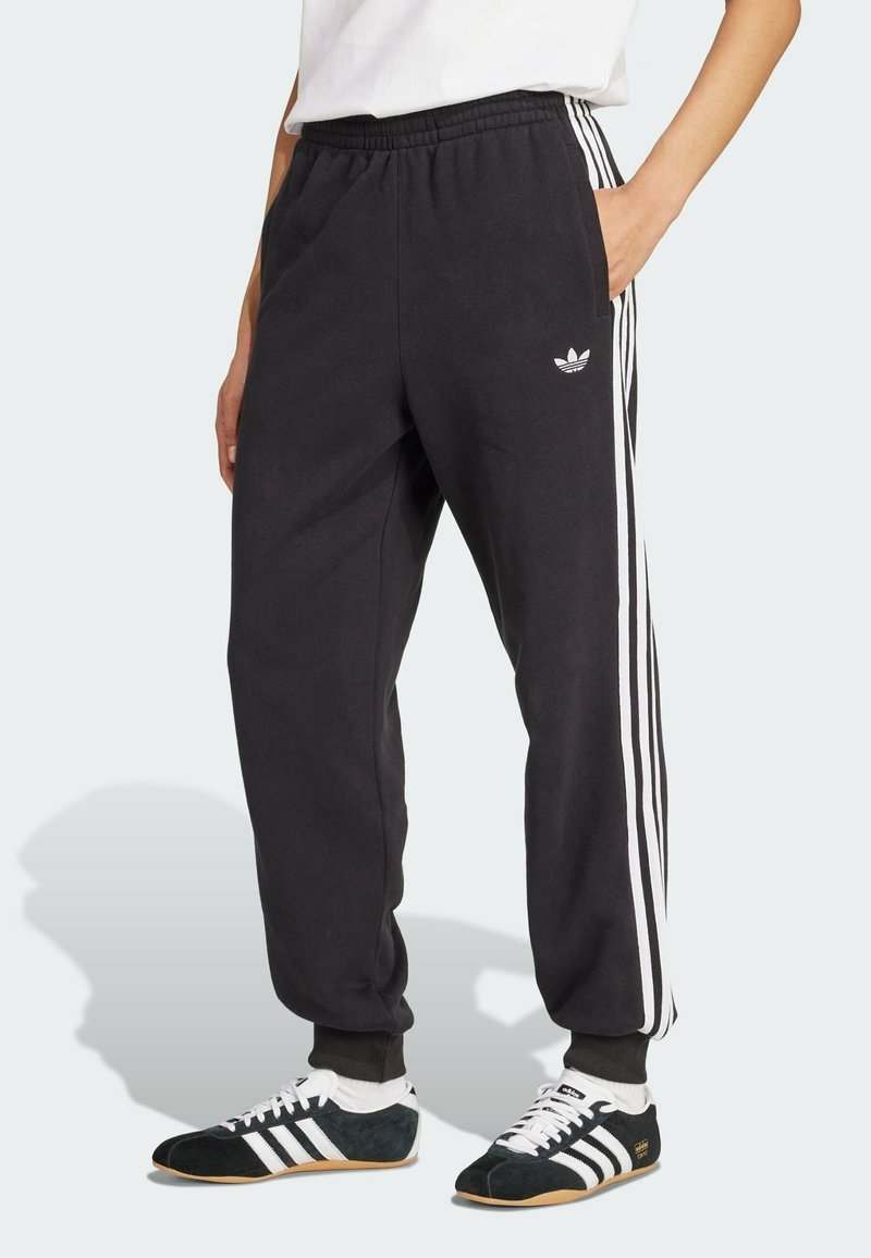 Crne fleece trenirke s bijelim bočnim prugama, elastičnim pojasom, bočnim džepovima i izvezenim logom na lijevom kuku.
