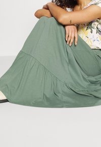 Groene gelaagde maxi-jurk gemaakt van zachte stof. Kenmerkt zich door een vloeiende stijl met een uitlopende onderkant en een minimalistischer ontwerp.