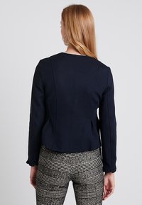 Námořnická modrá zkrácená bunda s dlouhými rukávy, texturovaný materiál, ševové detaily na zádech, kombinováno s kostkovanými kalhotami.