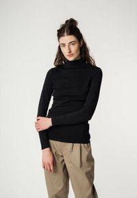 Schwarzes Langarm-Turtleneck-Shirt mit figurbetontem Design und glatter Textur; kombiniert mit beigen, hochgeschnittenen Hosen.