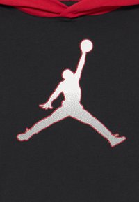 Sweat à capuche noir avec une capuche rouge présentant un grand logo Jumpman en argent réfléchissant dans une pose dynamique, mettant en valeur le mouvement athlétique.