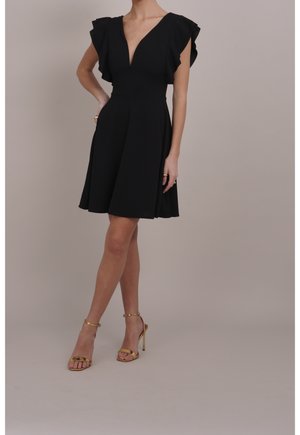 Vestido negro con escote en V profundo, mangas volante y falda acampanada. Combinado con tacones dorados con correa en el tobillo. Textura suave, longitud hasta la rodilla.
