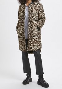 Leopardmønstret frakke med en afslappet pasform, der har to sidelommer, sorte ribbede manchetter og knaplukning. Båret over en lys skjorte og bukser.